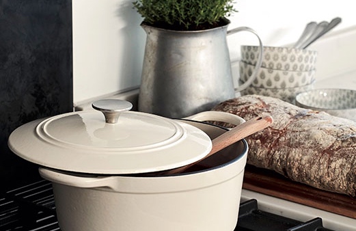 Cream stoneware pot on stove with kitchen utensils nearby