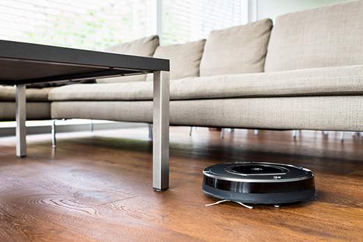 Robot vacuum cleaning wood floor under cream sofa