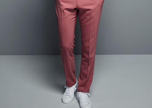 Male model wearing salmon pink trousers against grey backdrop