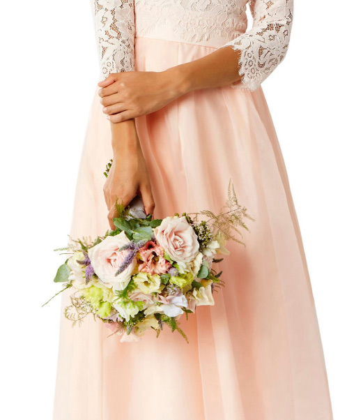 Close up of woman wearing a pale pink lace dress holding a wedding bouquet of flowers